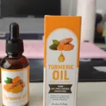 Frasco de vidrio ámbar con gotero junto a su caja naranja de aceite de cúrcuma de 30 ml para rostro y cuerpo, sobre una superficie de escritorio.