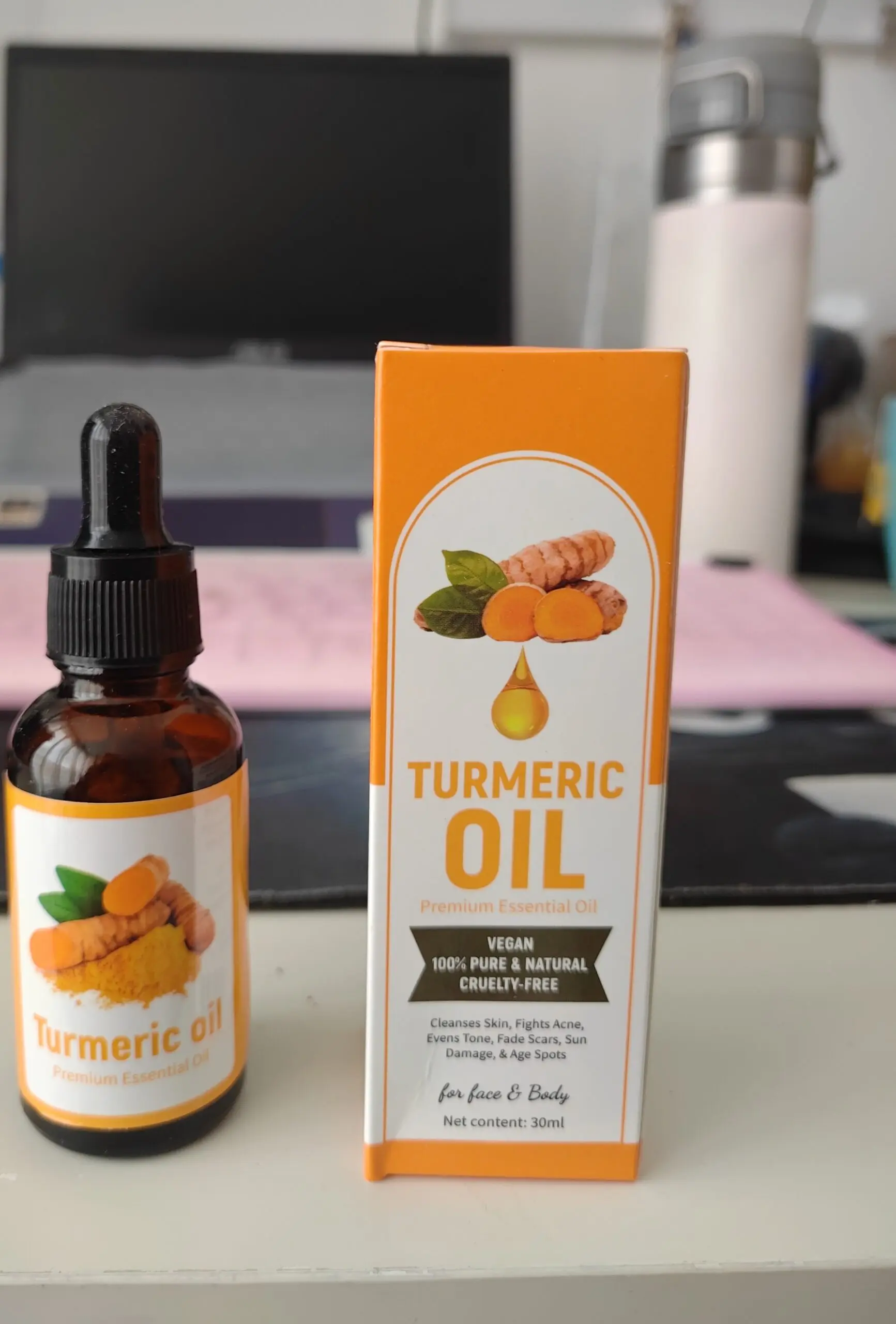Frasco de vidrio ámbar con gotero junto a su caja naranja de aceite de cúrcuma de 30 ml para rostro y cuerpo, sobre una superficie de escritorio.
