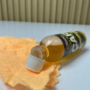 Botella de shampoo para auto con cera líquida y espuma acostada sobre un paño de microfibra naranja en una superficie blanca