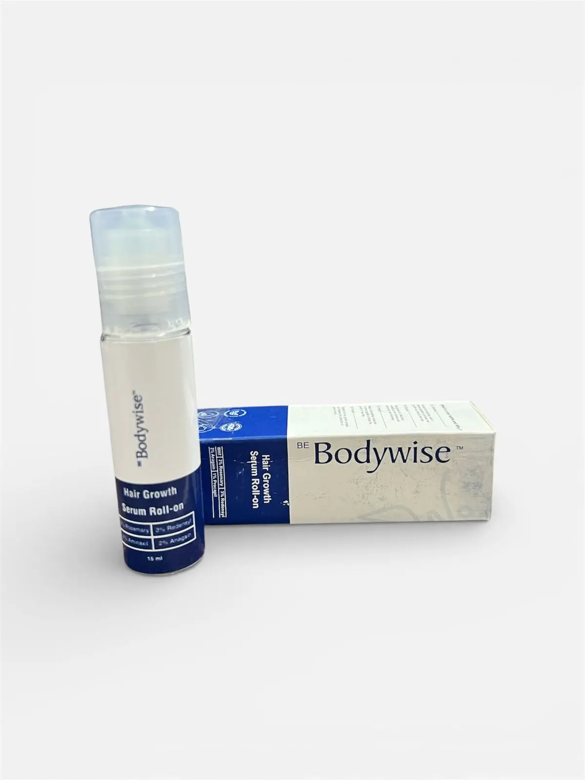 Serum roll-on Bodywise con aplicador para crecimiento capilar junto a su caja blanca y azul sobre fondo neutro.