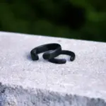 Set de dos anillos negros mate ajustables para magnetoterapia, sobre una superficie de piedra gris con fondo natural desenfocado.