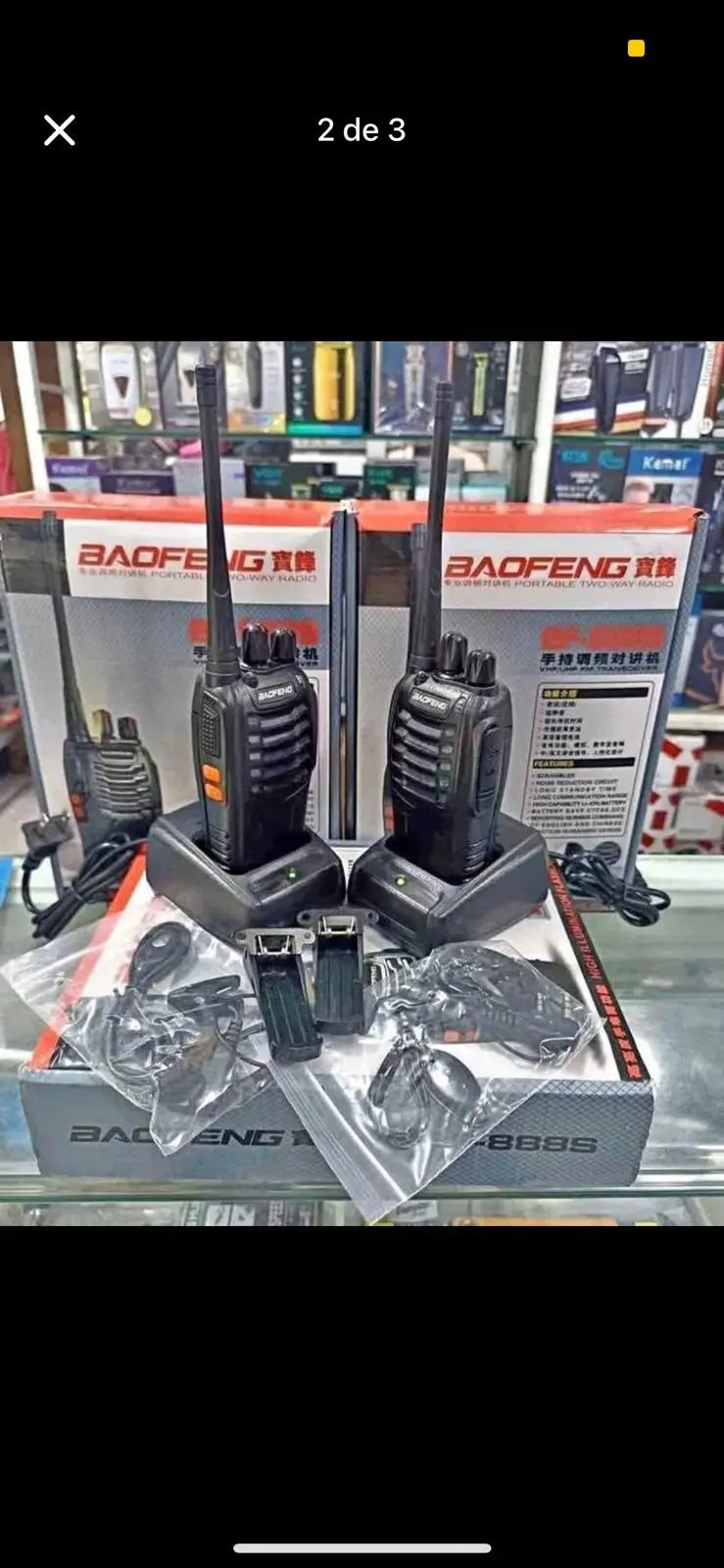 Par de radios portátiles Baofeng negros en sus bases de carga sobre cajas, con dos audífonos y accesorios en bolsas plásticas.