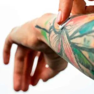 Persona aplicando bálsamo hidratante y protector sobre un tatuaje colorido en el antebrazo.