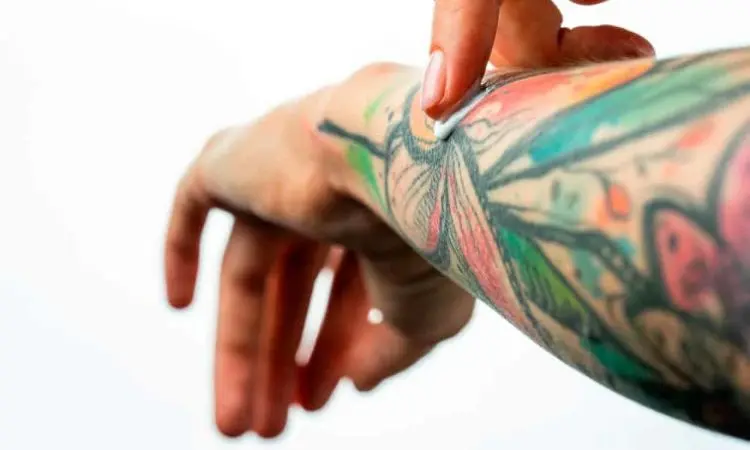 Persona aplicando bálsamo hidratante y protector sobre un tatuaje colorido en el antebrazo.