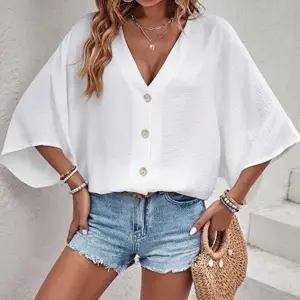 Blusa blanca de cuello V con botones frontales y mangas anchas, de tela ligera, combinada con shorts de denim para un look veraniego casual.