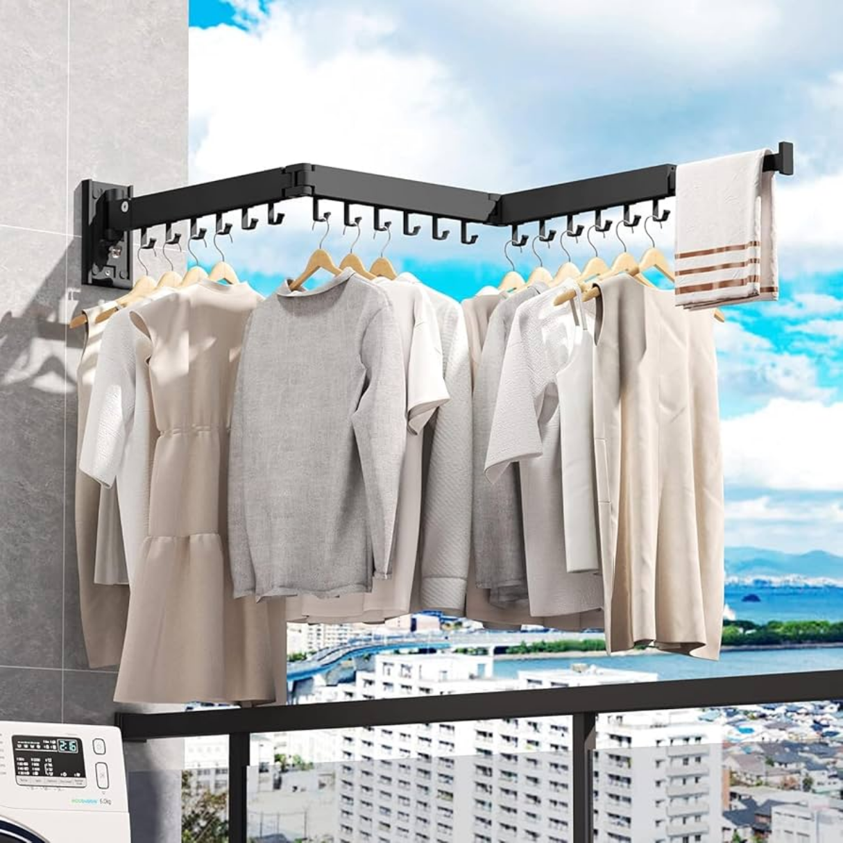 Tendedero extensible de metal negro anclado a pared con ganchos para perchas, mostrando ropa colgada en un balcón con vista a la ciudad.