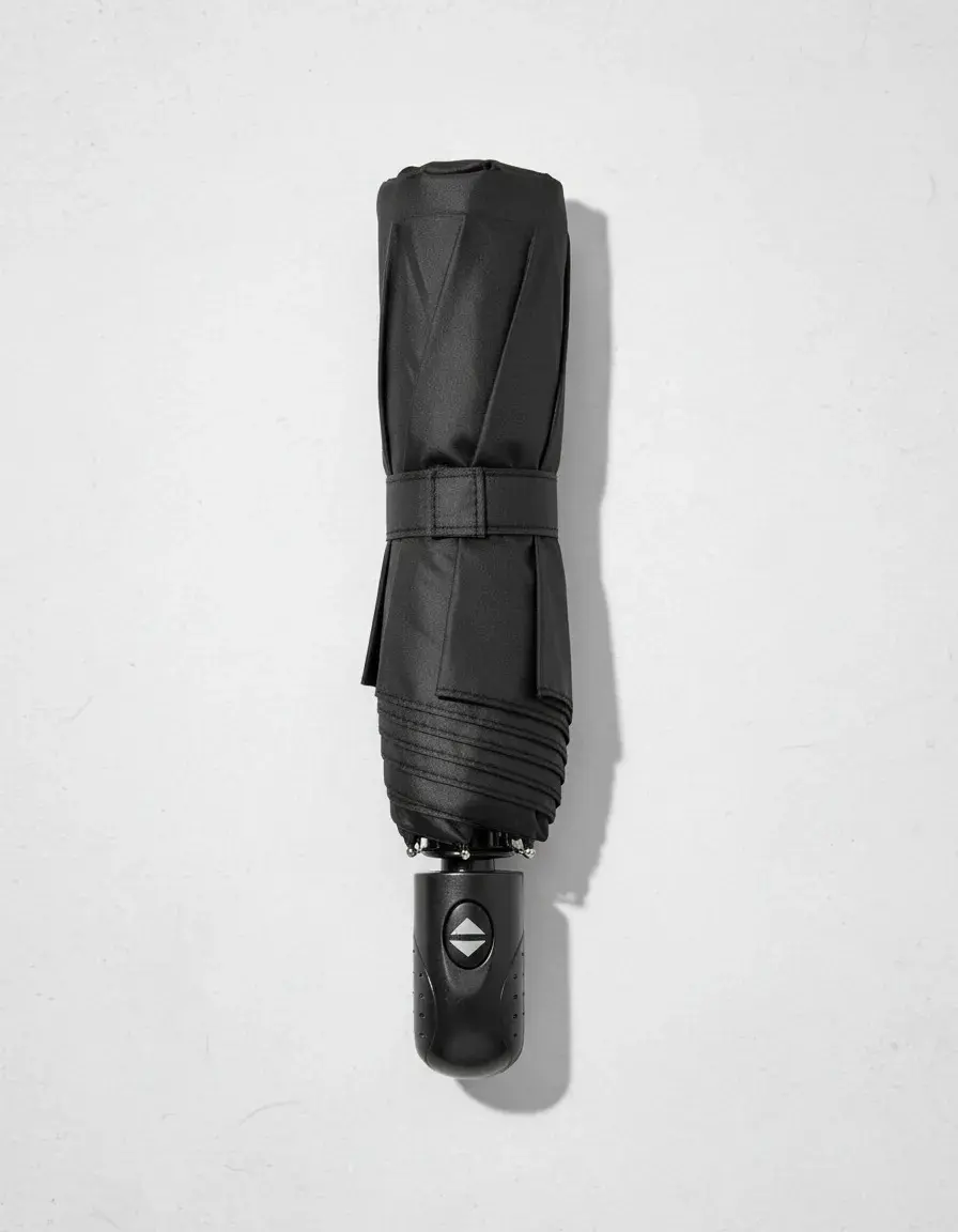 Sombrilla compacta negra cerrada con mango ergonómico y botón automático de apertura y cierre, vista vertical sobre fondo blanco.