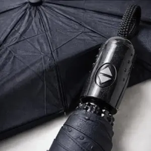 Sombrilla automática compacta negra con mango de botón y tela resistente, vista en ángulo para resaltar su mecanismo y textura.
