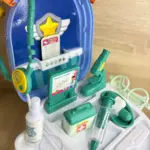 Maleta de doctor portátil azul abierta con accesorios médicos de juguete verdes y blancos, estetoscopio, jeringa, microscopio y monitor gráficos.