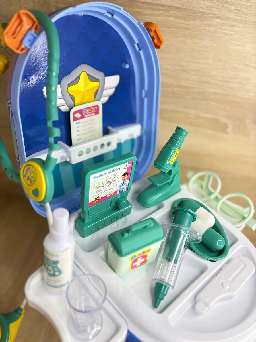Maleta de doctor portátil azul abierta con accesorios médicos de juguete verdes y blancos, estetoscopio, jeringa, microscopio y monitor gráficos.