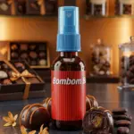 Atomizador corporal Bombom Bum en frasco ámbar con etiqueta roja y tapa azul, rodeado de bombones de chocolate y granos de café.