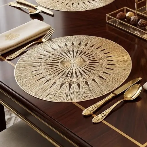 Individual redondo de PVC sintético dorado con diseño de radios sobre mesa de madera oscura con cubiertos y servilleta.