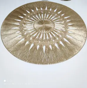 Individual de mesa redondo dorado en PVC sintético con diseño de radios y entramado detallado, sobre superficie blanca.
