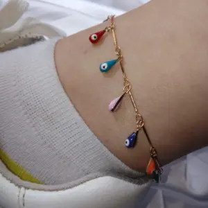 Tobillera dorada con dijes colgantes en forma de gota multicolor y diseño de ojo turco, usada sobre calcetín blanco y zapatilla.