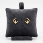 Aretes topitos de acero inoxidable dorados con diseño de gato en luna sobre un cojín de terciopelo gris oscuro.