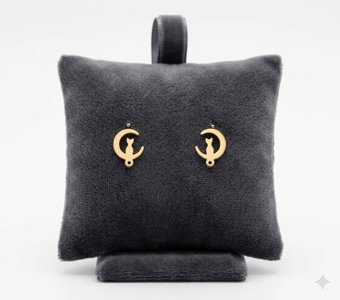 Aretes topitos de acero inoxidable dorados con diseño de gato en luna sobre un cojín de terciopelo gris oscuro.