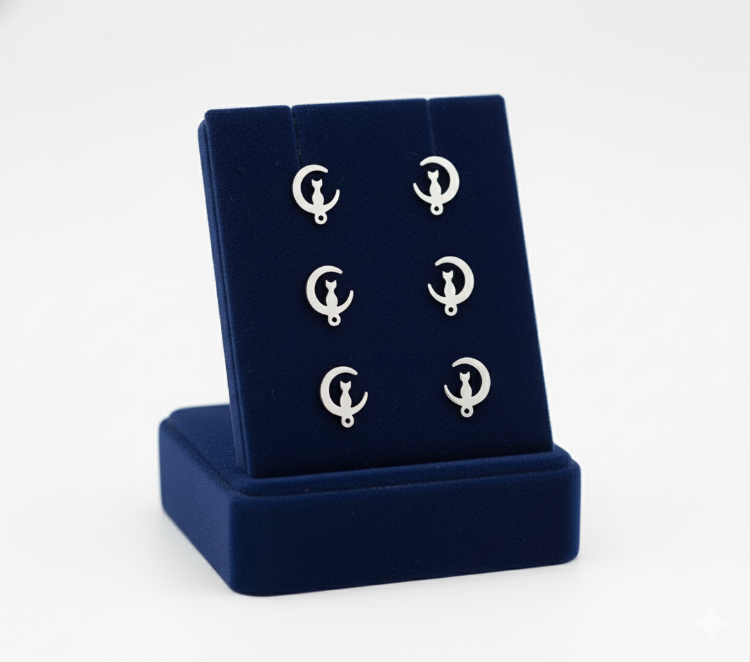 Aretes de acero inoxidable plateados con diseño de gato en luna creciente, exhibidos en un soporte de terciopelo azul marino.