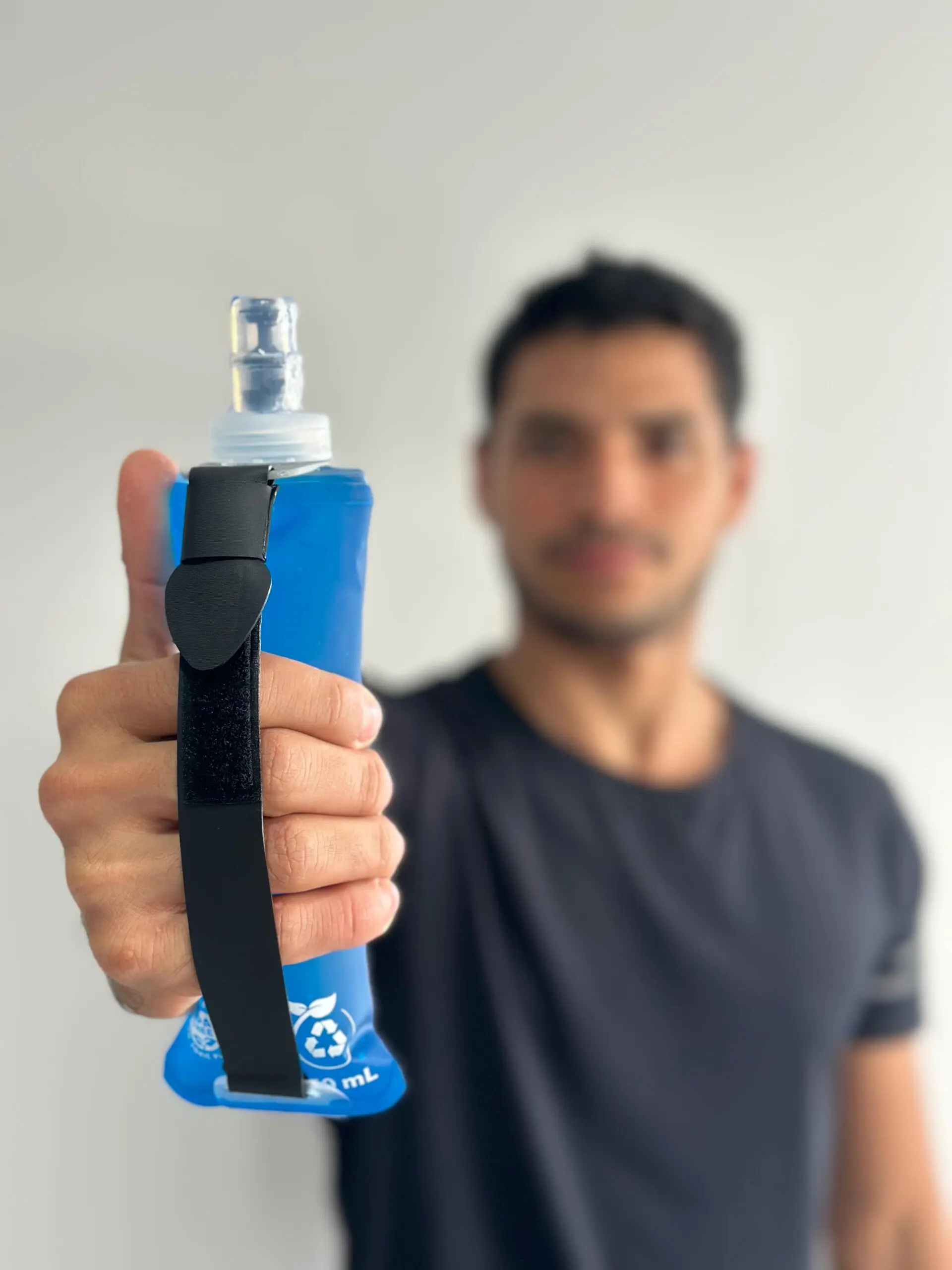 Termo plegable azul con correa negra para deporte, sostenido en primer plano por una mano, resaltando su diseño flexible y compacto.