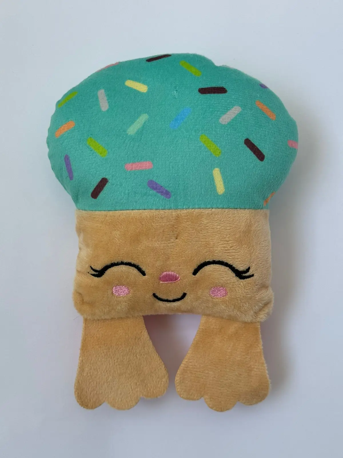 Peluche Moofie de textura suave, con parte superior turquesa con chispas de colores y base beige con rostro de perro sonriente y mejillas rosadas.