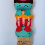 Peluche alargado con tres personajes de postres apilados en colores azul, rojo y beige, con detalles de chispas y rostros sonrientes.