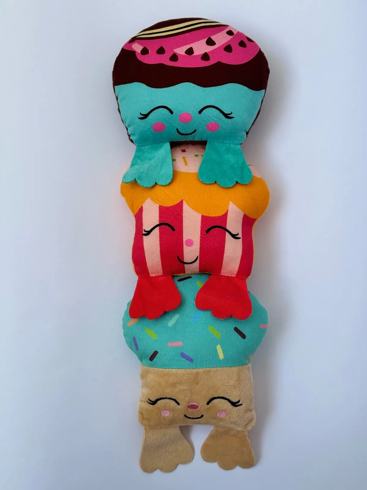 Peluche alargado con tres personajes de postres apilados en colores azul, rojo y beige, con detalles de chispas y rostros sonrientes.