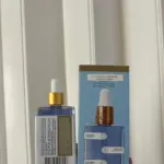 Frasco de vidrio azul texturizado con gotero dorado y su caja celeste ilustrada con notas de fresa, vainilla y ámbar.