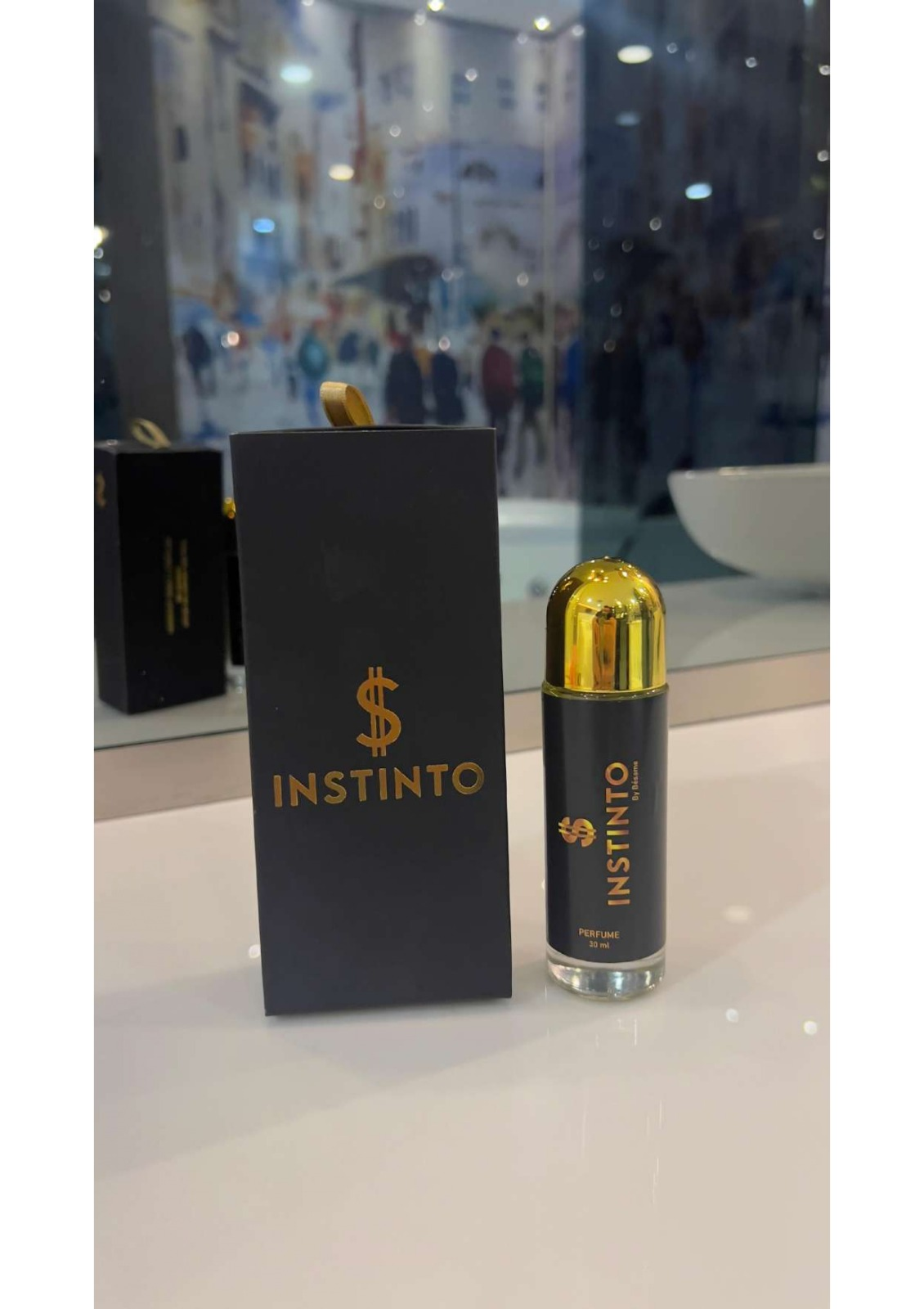 Perfume masculino Instinto de 55 ml con envase cilíndrico negro, tapa dorada y caja a juego con logo de dólar, sobre superficie blanca reflectante.