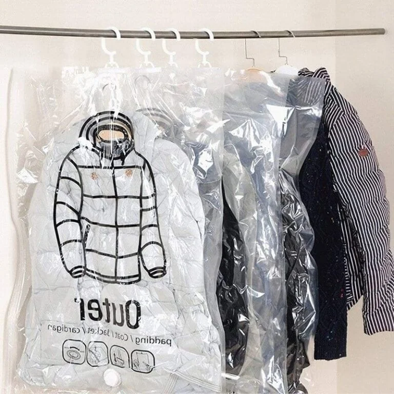 Bolsas de compresión colgantes transparentes para organizar el armario, con una chaqueta blanca acolchada y prendas oscuras en ganchos blancos.