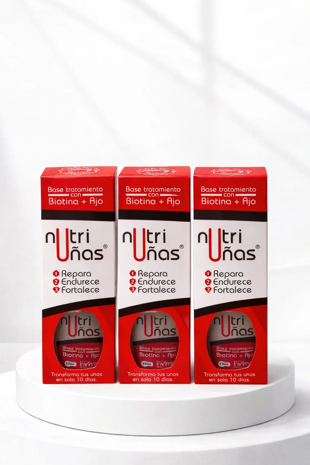 Tres cajas rojas y blancas de base tratante Nutriuñas con biotina y ajo, alineadas sobre una base circular blanca.