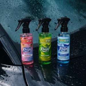 Tres ambientadores vehiculares Flux Car con atomizador en aromas tropical, té verde y oceánico sobre la superficie mojada de un automóvil.