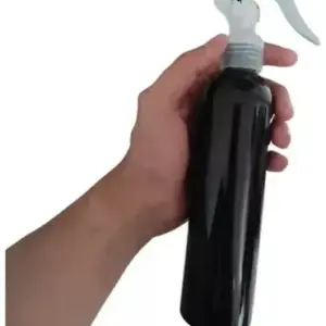 Mano sosteniendo botella rociadora negra brillante con atomizador blanco para aromaterapia de sábanas.