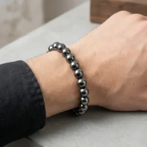 Pulsera de hematita natural gris brillante con esferas redondas en nylon, puesta en la muñeca de un hombre con camisa negra.