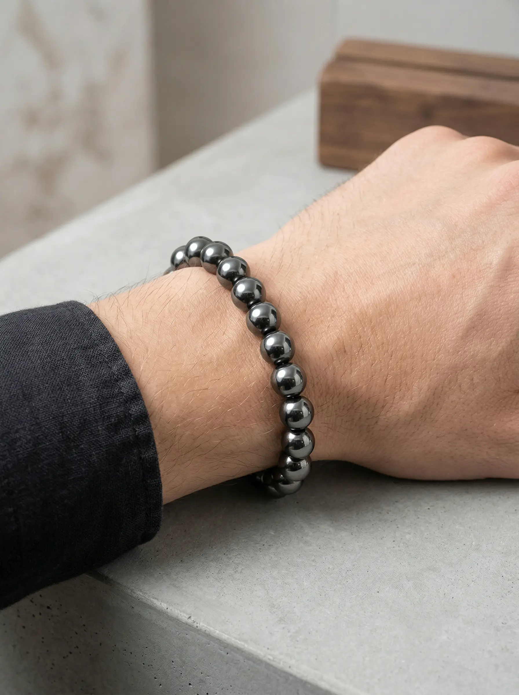 Pulsera de hematita natural gris brillante con esferas redondas en nylon, puesta en la muñeca de un hombre con camisa negra.