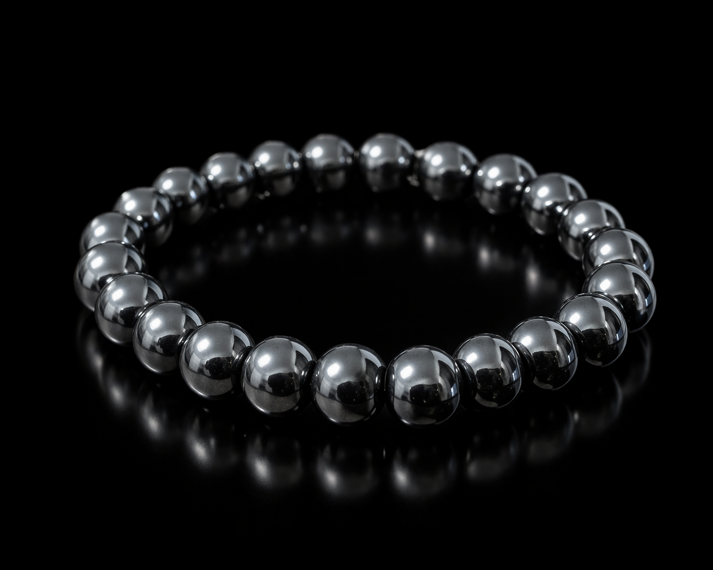 Pulsera de hematita natural con cuentas esféricas de acabado gris metálico brillante, en forma circular sobre fondo negro con reflejo.