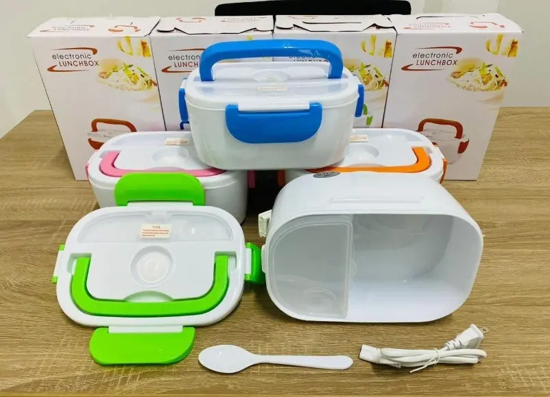 Loncheras eléctricas portátiles con cajas, incluyendo unidades en colores azul, rosa, verde y naranja, con cuchara y cable de alimentación sobre mesa.