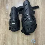 Par de protecciones negras para moto de alto impacto, una rodillera grande y una codillera más pequeña con ventilación y correas ajustables sobre madera.