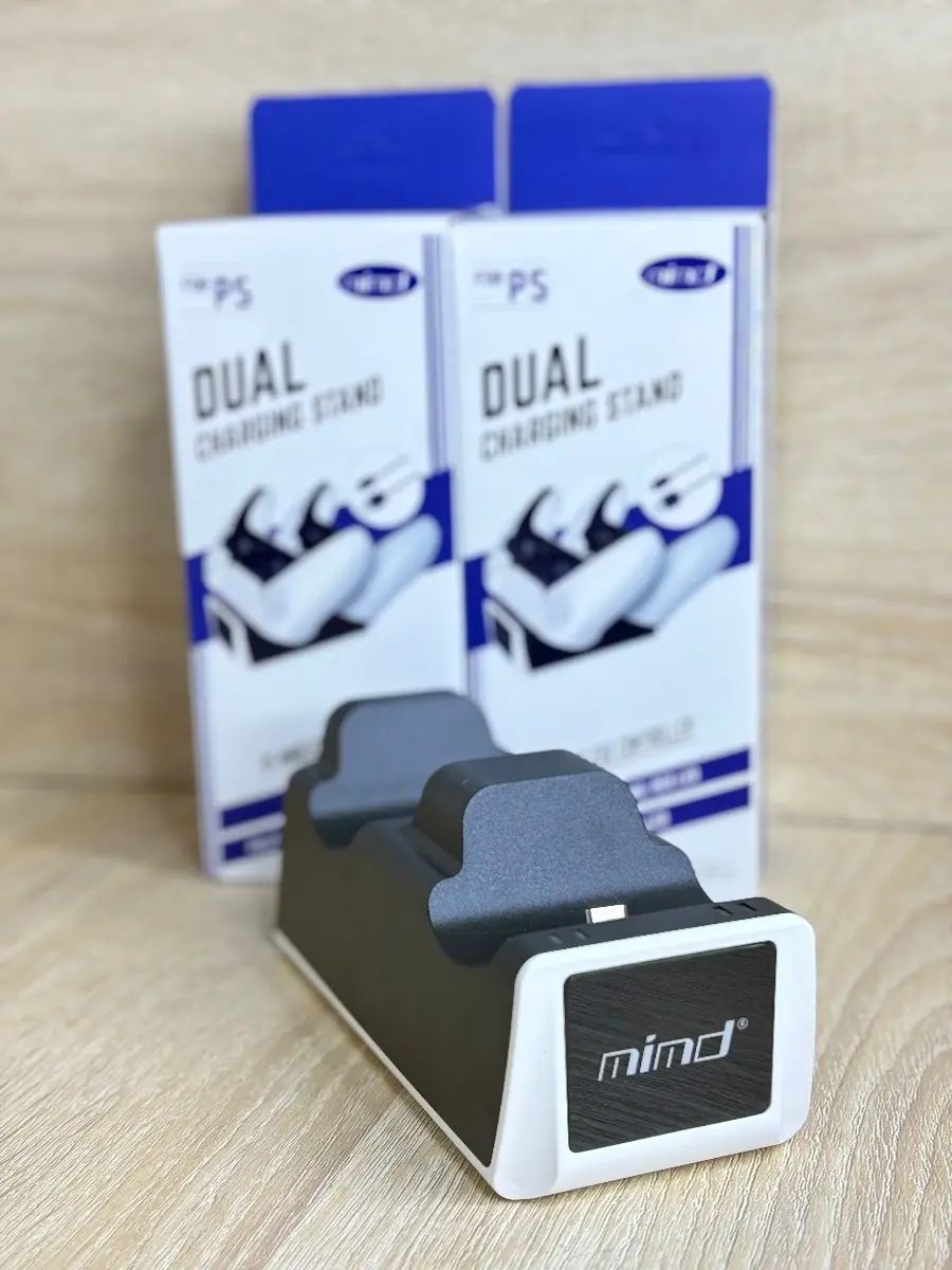 Cargador dual mimd para controles, color negro con bordes blancos, junto a sus cajas de empaque sobre una superficie de madera clara.