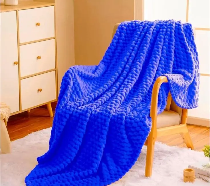 Cobija azul vibrante con textura de nudos gruesos tejida a mano, extendida sobre una silla de madera en un ambiente acogedor.