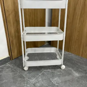 Carrito organizador de metal blanco de tres niveles con bandejas de malla y una superior sólida, con cuatro ruedas para fácil movilidad.