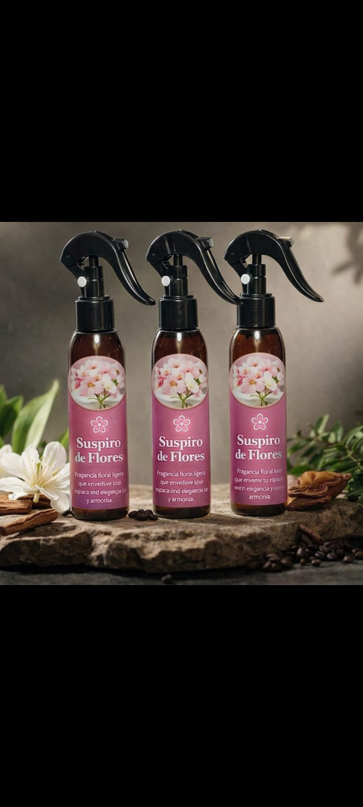 Tres botellas plásticas ámbar de atomizador con etiqueta rosa Suspiro de Flores sobre roca, rodeadas de flores blancas y granos de café.