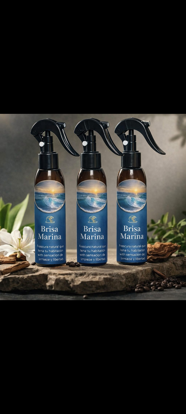 Tres botellas oscuras con atomizador negro de Brisa Marina dispuestas en fila sobre una superficie de piedra con flores blancas y hojas.