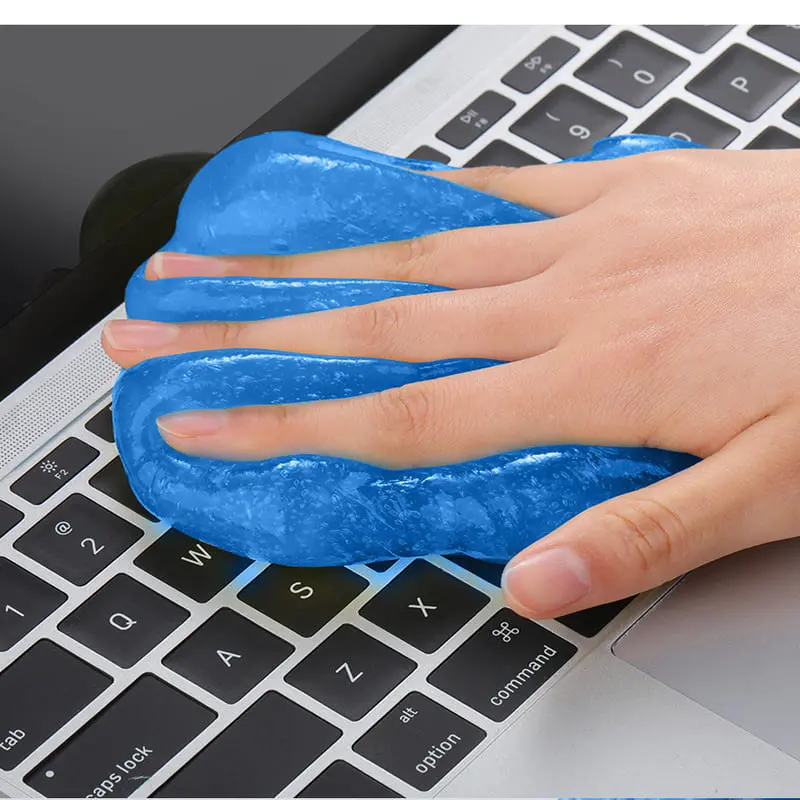 Mano presionando gel limpiador adhesivo azul sobre el teclado de una laptop para remover polvo y suciedad en espacios estrechos
