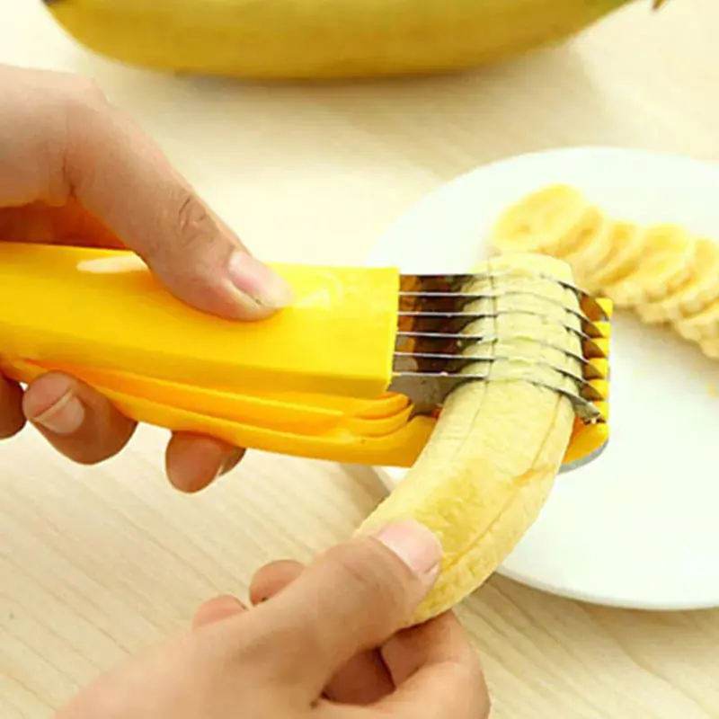 Rebanador de banano amarillo con cuchillas de acero inoxidable cortando rodajas uniformes de un banano pelado sobre un plato blanco.