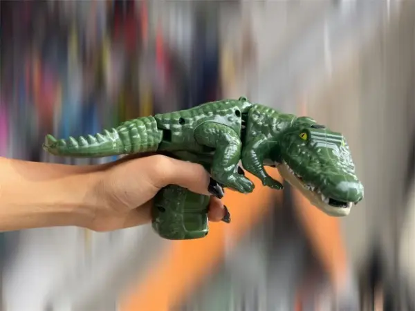 Mano sosteniendo un cocodrilo de juguete verde articulado con textura escamosa y detalles en relieve para juego infantil.