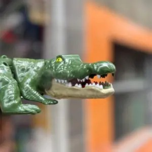 Cocodrilo de juguete verde articulado con cabeza texturizada y fauces abiertas mostrando dientes blancos.
