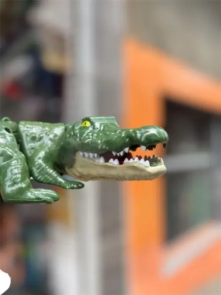 Cocodrilo de juguete verde articulado con cabeza texturizada y fauces abiertas mostrando dientes blancos.