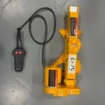 Gato hidráulico eléctrico 12V automático color amarillo con control remoto negro de dos botones, sobre piso de baldosa gris.