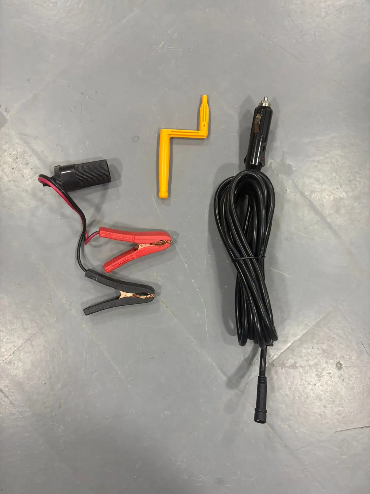 Accesorios de gato hidráulico eléctrico 12V: cable adaptador de encendedor, pinzas para batería rojas y negras y manivela manual amarilla.