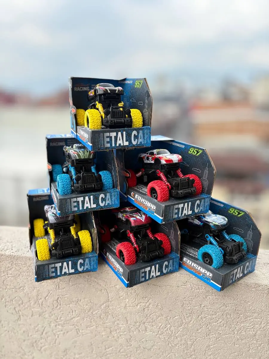 Seis carros todoterreno a escala con ruedas grandes de colores amarillo, azul y rojo, apilados en sus cajas azules de la marca Metal Car.