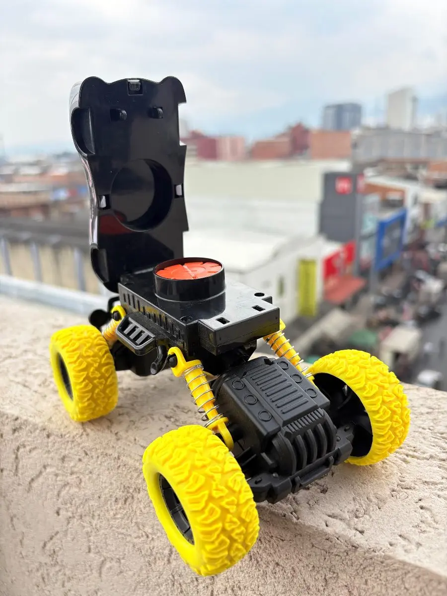 Carro todoterreno a escala negro con llantas amarillas texturizadas, resortes expuestos y compartimento superior abierto que revela un lanzador de discos blandos rojo.